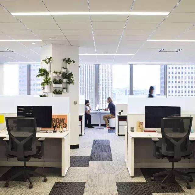 贝博体彩app一座办公大楼的室内场景, 前景有几张桌子，两个人在大窗户前的一张桌子前工作.